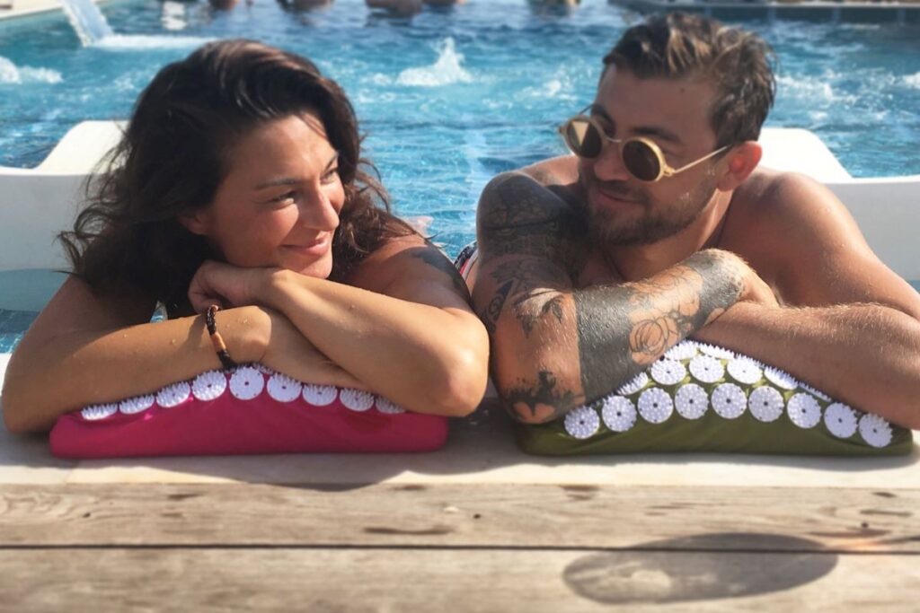 People laying on bed of nails product outside in front of a pool