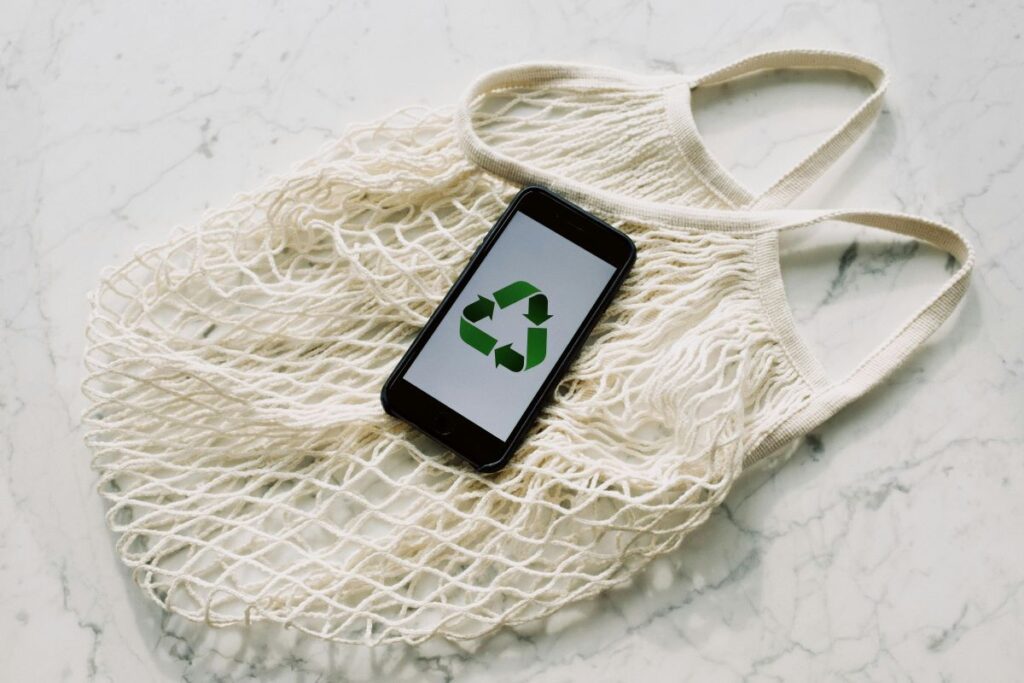 Reusable bag with a phone sitting on top displaying a recycle symbol.
